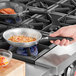 A person cooking food in a Vollrath Wear-Ever aluminum fry pan with a black handle.