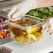 A person in gloves holding a Choice clear polycarbonate food pan filled with pickles.