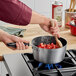 A person stirring strawberries in a Vollrath Wear-Ever sauce pan on a stove.
