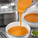 A Breville Commercial blender pouring orange liquid into a bowl of soup.