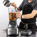 A man in an apron using a Breville commercial blender on a counter to make a drink.