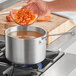 A person pouring cut carrots into a Vollrath Wear-Ever Classic Select aluminum sauce pan on a stove.