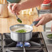 A person stirring green vegetables in a Vollrath stainless steel sauce pan.