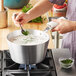 A person stirring green soup in a Vollrath sauce pan on a gas stove.