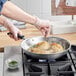 A person cooking chicken in a Vollrath stainless steel fry pan on a stove.