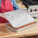 A woman holding a Western Plastics full size foil steam table pan lid over a tray of food.