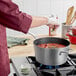A person cooking tomato sauce in a Vollrath Wear-Ever sauce pan on a stove.