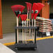 A SPC Retail long handle tool cart with red and black handles holding rakes and bags of sand.