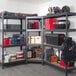 A metal AR Shelving boltless corner shelving unit with fiberboard shelves holding various items.