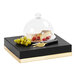 A black and gold Cal-Mil square display riser holding plates of cheese and fruit on a table.
