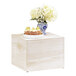 A white wooden display riser with a blue and white vase of flowers and a cupcake.