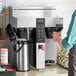 A person using a Fetco twin automatic digital coffee brewer to make coffee.