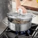 A person using a Vigor stainless steel stock pot to cook food on a stove top.