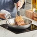 A person cooking a piece of meat in a Vigor stainless steel fry pan.