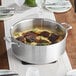 A Vigor stainless steel brazier with meat and mashed potatoes on a table.