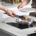 A person using Vigor SS3 Series 8" Tri-Ply Stainless Steel Fry Pan to cook food.
