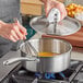 A hand stirring a Vigor stainless steel sauce pan on a stove with a whisk.