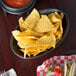 An oval charcoal polyethylene basket filled with tortilla chips and a bowl of salsa on a table.