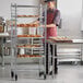 A woman in a chef's uniform standing next to a Regency side load sheet pan rack filled with doughnuts.