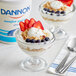 A glass bowl of Dannon non-fat plain yogurt with strawberries and oat flakes.