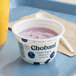 A plastic container of Chobani blueberry Greek yogurt on a white tray with a spoon.