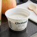 A close-up of a white Chobani Non-Fat Plain Greek Yogurt container on a table next to a spoon and apple.