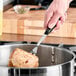 A hand holding a Vollrath stainless steel pot fork with a black handle over a pot of meat.