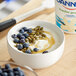 A close up of a bowl of Dannon Low-Fat Vanilla Yogurt with blueberries and pumpkin seeds.