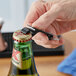 A hand holding a Choice black aluminum bottle opener opening a bottle of beer.