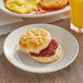 A plate with a Bakery Chef buttermilk biscuit with jam on it next to a glass of juice.