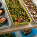 A yellow Cambro market pan on a table with a tray of food including green beans, broccoli, and salmon.