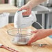 A person using a white Hamilton Beach hand mixer to mix ingredients in a bowl.