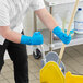 A man in blue Ansell AlphaTec gloves mopping a floor in a school kitchen.