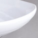 A close-up of a white Carlisle square melamine plate with a curved edge.