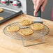 A person using a spatula to put cookies on a Choice round cooling rack.