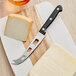 An Acopa stainless steel cheese knife cutting cheese on a cutting board.