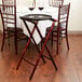 A Lancaster Table & Seating mahogany folding tray stand with a white table cloth on a table with wine glasses.
