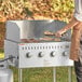 A person cooking food on a Backyard Pro stainless steel outdoor grill in the grass.