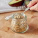 A person using a spoon to put mixed seeds into a Choice glass storage jar.