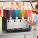 A quadruple 5-gallon bowl refrigerated beverage dispenser with four separate containers holding different colored drinks.