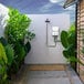 An Eccotemp portable outdoor tankless water heater used in an outdoor shower next to a wall with plants.