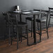 A Lancaster Table & Seating black cast iron bar height end column table base with chairs and menus.