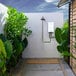 An Eccotemp outdoor tankless water heater next to a shower with green plants.
