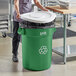 A woman in a kitchen putting a white lid on a green Lavex recycling can.