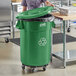 A woman in a school kitchen putting recycling into a green Lavex recycling can.