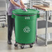 A woman in a school kitchen putting a Lavex green recycling can into a container.