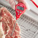 A person using a CDN red waterproof digital pocket probe thermometer to check the temperature of meat.