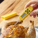 A hand holding a yellow Taylor digital pocket thermocouple thermometer with a screen over a chicken.