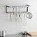 A Regency stainless steel wall mounted double line pot rack with kitchen utensils hanging from it.