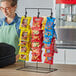 A woman standing behind a freestanding chip rack full of snacks.